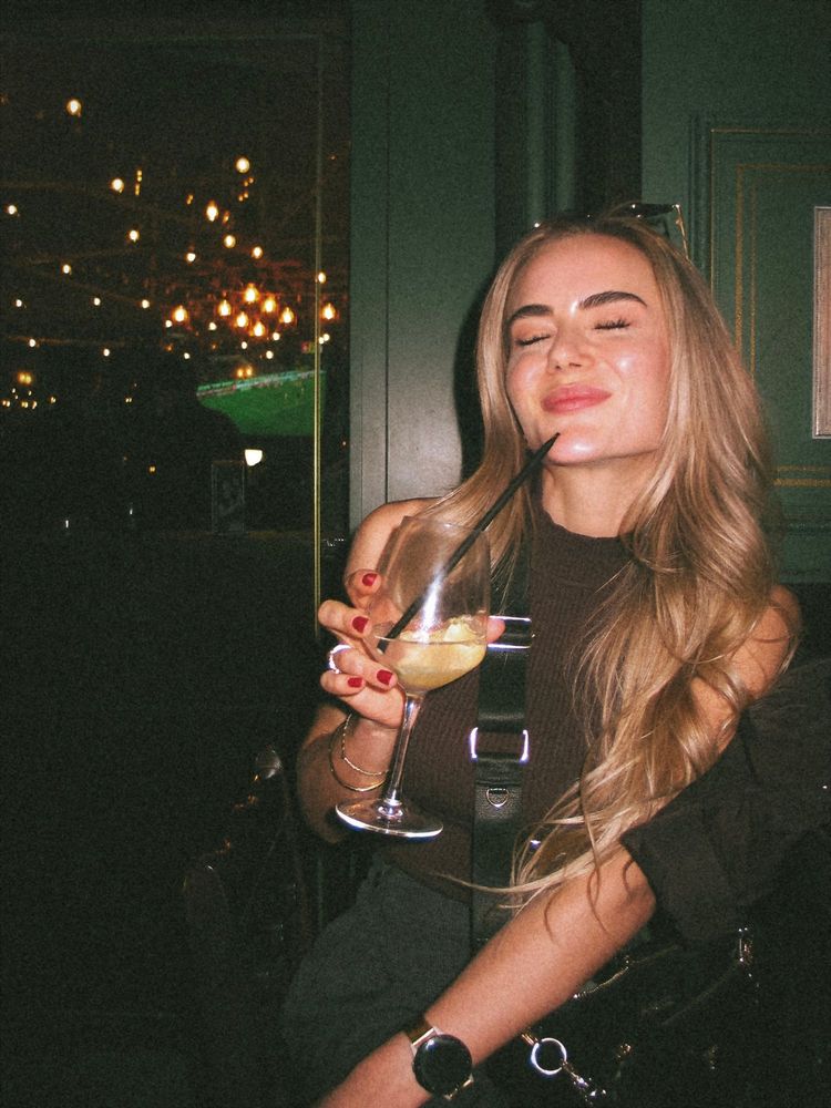 Stella lacht mit einem Drink in einer Bar